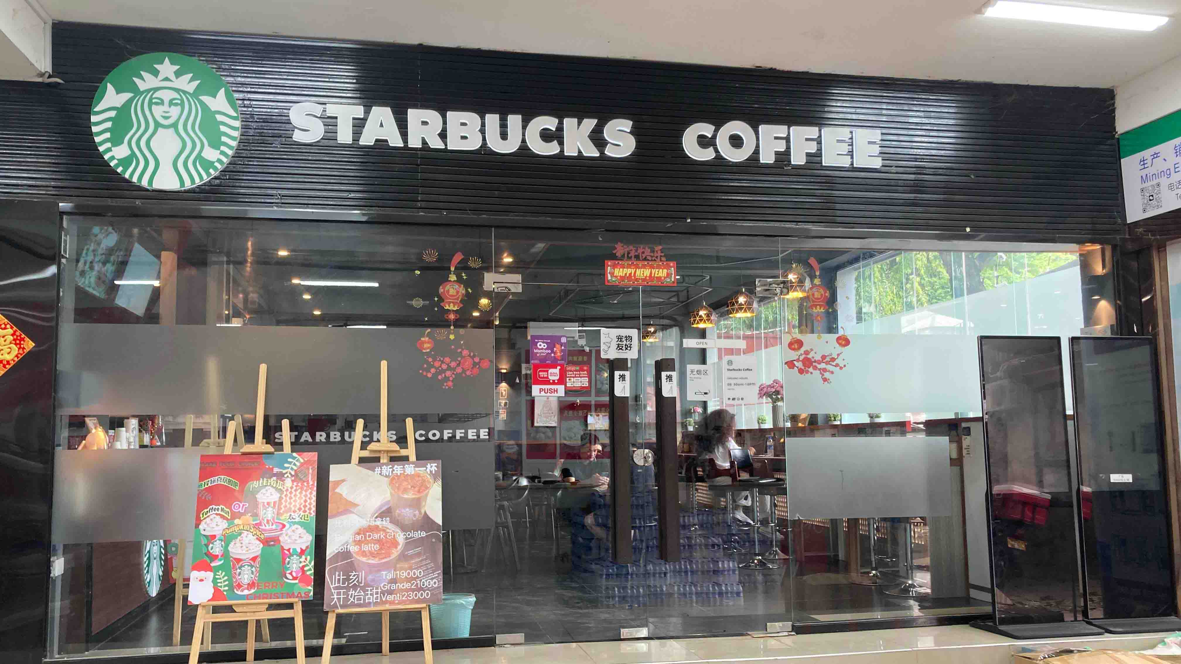 Front view of the Starbucks entrance decorated with holiday posters, transparent doors, and a visible seating area inside.
