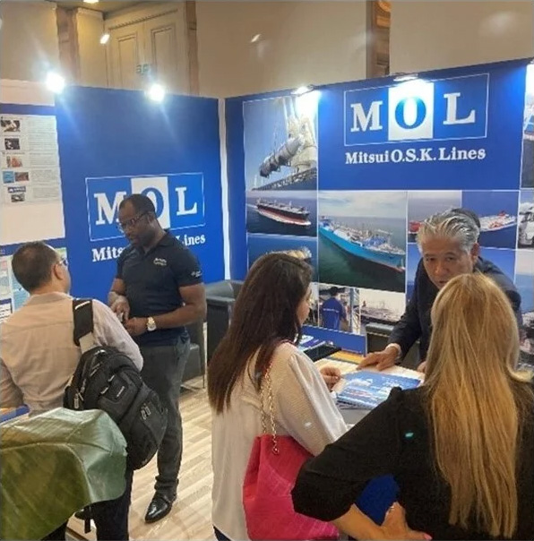 MOL（商船三井）の担当者が展示会ブースで来場者と対話している様子。海運に関するビジュアルが展示されている。