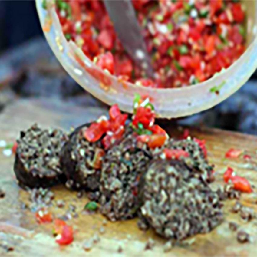 木のまな板の上に並べられたムトゥラソーセージの断片。トマトと玉ねぎの刻み具がのっている。